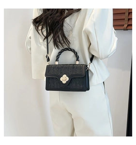 Detail of black woven crossbody bag featuring a golden floral clasp and twisted handle