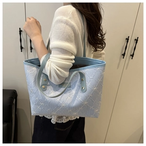 Close-up of light blue tote bag featuring white floral embroidery and gold rivets