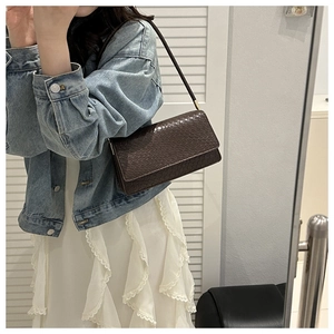 Detailed view of deep brown crocodile pattern handbag styled with a denim jacket