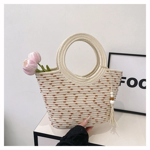Détail du sac cabas en paille tressée à la main avec poignées rondes et gland en perles