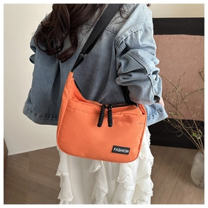 Détail du sac bandoulière orange montrant l'étiquette mode et la texture en nylon