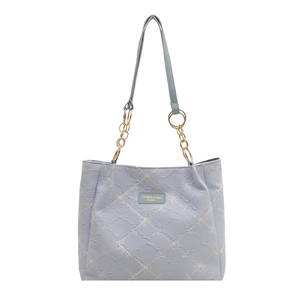 Light blue quilted tote bag with floral patterns and gold chain straps on white background