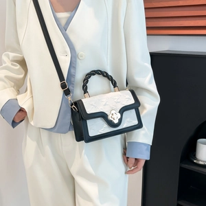 Detail of a chic black and white flap bag with golden flower lock and braided handle
