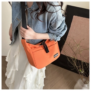 Détail de la sacoche orange en nylon avec étiquette FASHION et tirette de zip tissée