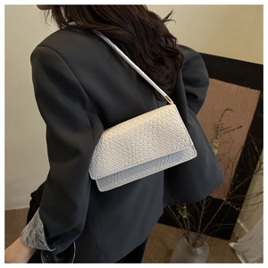 Close-up of white woven shoulder bag with gold hardware worn by a model in a grey suit