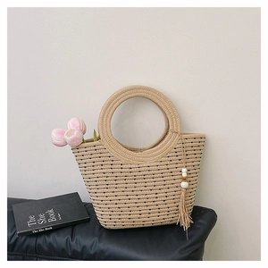 Détail du sac seau en paille tressée à pois noirs avec poignée ronde et pompon en perles bois