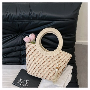 Détail du sac seau en paille beige avec grande poignée ronde et pompon en perles
