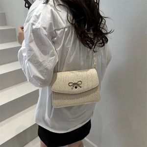 Détail du sac bandoulière tissé crème avec fermoir nœud doré sur un escalier blanc