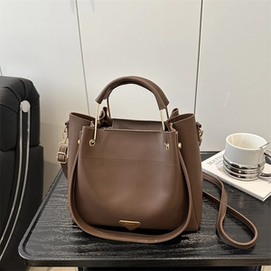 Minimalist dark brown leather bucket bag with top handle and gold logo on wooden table