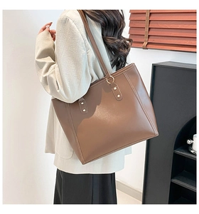 Detail of dark brown tote bag with metal rivets on a woman in a white blazer
