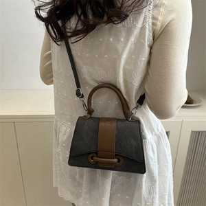 Textured dark gray square crossbody bag with brown leather handles on a white lace dress