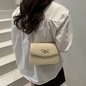 Détail d'un sac bandoulière tissé avec fermoir nœud doré porté par un mannequin en décor