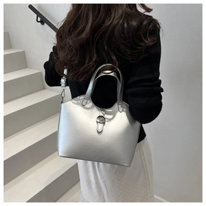 Silver metallic trapezoid handbag with dual round handles and detachable strap on white stairs