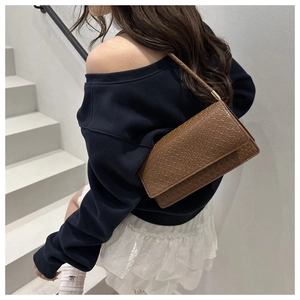 Deep brown croc-embossed underarm bag with flap closure styled on a model in nature