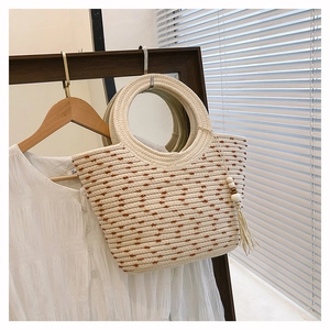 Détail du sac seau en paille tressée avec motifs à pois et pompon en perles de bois