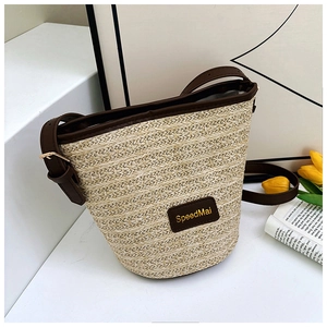 Dettaglio della borsa a secchiello in paglia intrecciata con tracolla in pelle e logo dorato