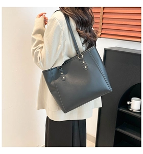 Minimalist black leather tote bag with gold ring hardware shown on a female model