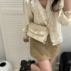 Détail d'un sac bandoulière tissé beige avec nœud en métal doré et rabat élégant