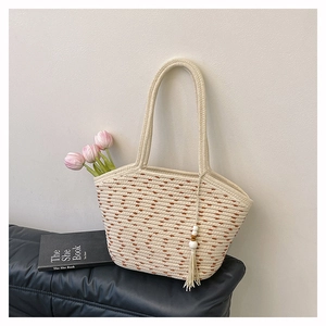 Detail of woven straw tote bag featuring white tassels with wooden beads on a black leather seat