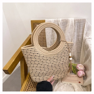 Détail du sac cabas en paille avec anse ronde, rayures noires et accessoire à pompon décoratif