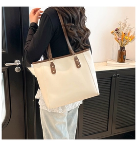 Close-up of beige tote bag with brown straps and gold metal ring hardware detail