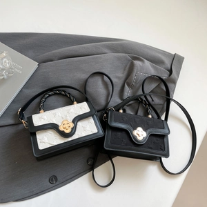 Detailed close-up of textured fabric crossbody bag with a golden floral lock and woven handle