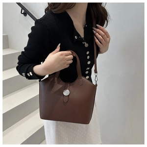 Detail of a brown leather shoulder bag with a silver buckle worn by a model in lifestyle shot