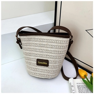 Dettaglio di una borsa a secchiello in paglia con tracolla in pelle marrone e logo chic