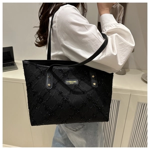 Detail of black tote bag with shimmering rhombic texture and brand logo on shoulder