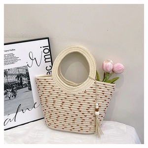 Détail du sac seau en paille tissée à pois marron avec pompon en perles de bois