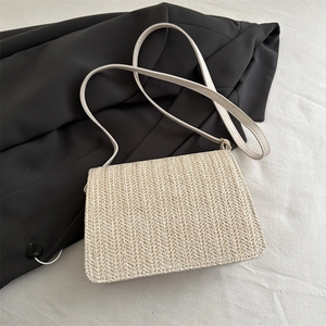 Détail d'un sac bandoulière tissé en paille blanc crème sur une veste de costume noire