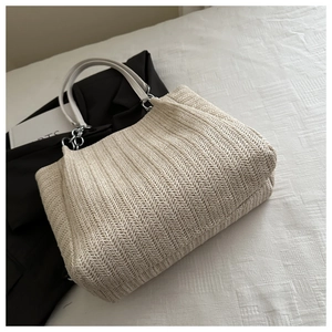 Close-up of cream straw tote bag featuring herringbone weave and white leather handles