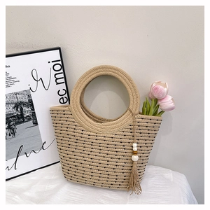 Détail d'un sac en paille tissée avec gland perlé et tulipes sur nappe blanche