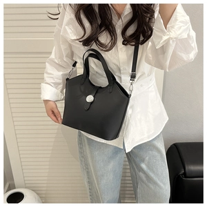 Detail of a matte black handbag with silver clasp worn with a white shirt and jeans
