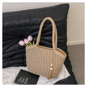 Detail of woven straw tote bag featuring black striped patterns and decorative tassel charm