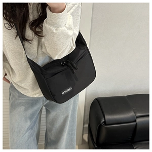 Sac bandoulière minimaliste en nylon noir porté par un mannequin en sweat à capuche