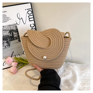 Détail d'un sac seau tressé beige avec un grand bouton perle central sur le rabat rond