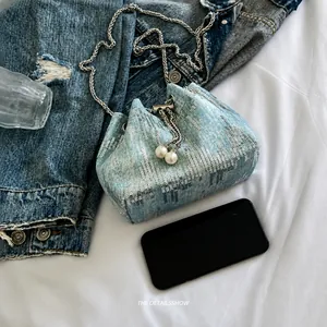 Detailed shot of light blue denim bucket bag featuring silver sequins and pearl drawstring