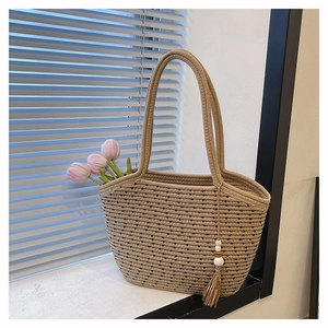 Detail of woven beige tote bag with black stripes and wooden bead tassel ornament