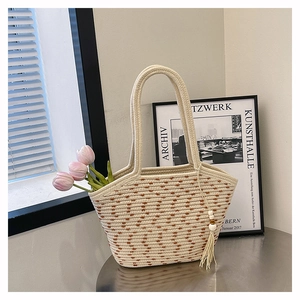 Detail of woven straw tote bag with brown heart patterns and tassel bead accent