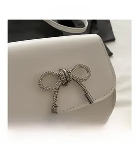 Detailed close-up of white leather handbag featuring a sparkling rhinestone butterfly buckle