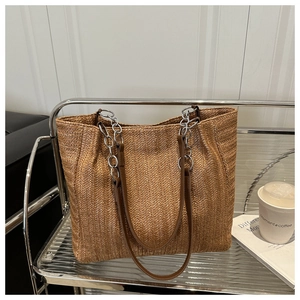 Detail of V-shaped straw tote bag with metal chain handle and leather strap textures