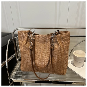 Detail of woven straw tote bag with brown herringbone pattern and metal chain strap