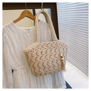 Detail of woven straw tote bag with brown polka dots and a wooden bead tassel charm
