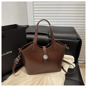 Detail view of premium dark brown leather handbag with round metal buckle and twin handles