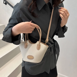 Sac seau tissé beige avec poignée en cuir porté par un mannequin en escalier