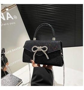 Detail of black glitter evening bag featuring a silver rhinestone bow and chain strap