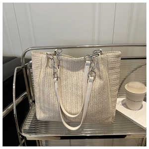 Detailed view of straw woven tote bag with herringbone texture and silver chain strap