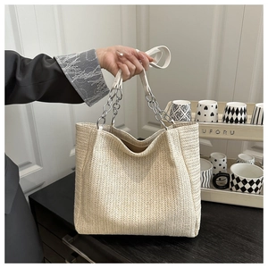 Close-up of beige woven straw tote bag with silver chain and white leather strap
