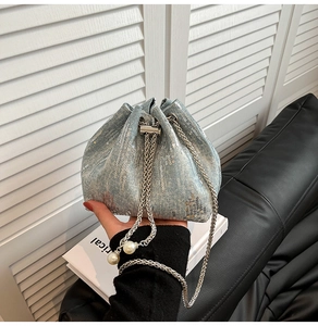Close-up of light blue denim bucket bag with silver sequins and pearl chain strap